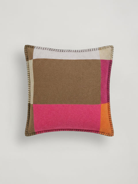 A square decorative throw pillow with a patchwork design in camel, bright pink, orange, and off-white, featuring a stitched border, shown against a neutral light gray background.