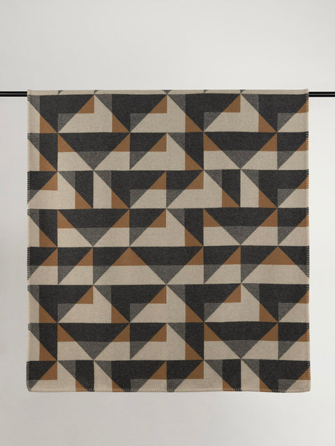 Brown, black and beige geometric pattern wool blanket against grey background.