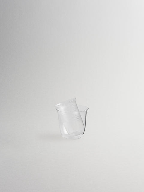 Small millerighe glass sidecar stacked inside clear glass ice bucket, shown on grey background.