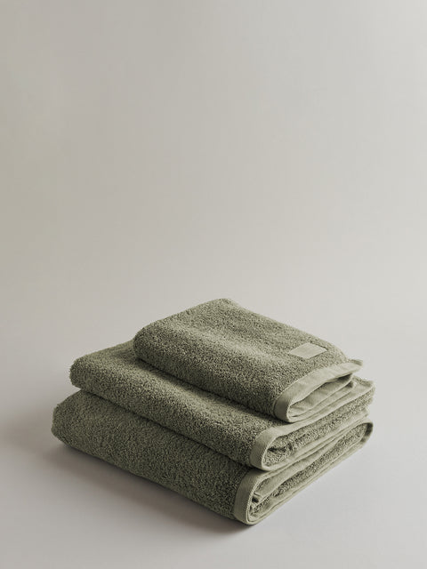Stack of three olive green towels on grey background.