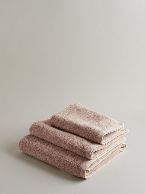 Stack of three light pink towels on grey background.