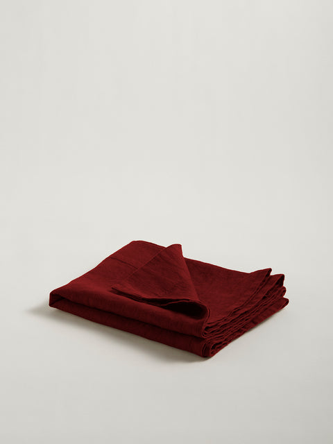 A folded rich red linen table runner shown on grey background.