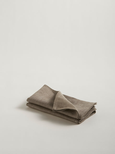 A stack of two folded dark beige linen napkins, on grey background.
