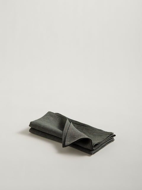 A stack of two folded olive green linen napkins, on grey background.
