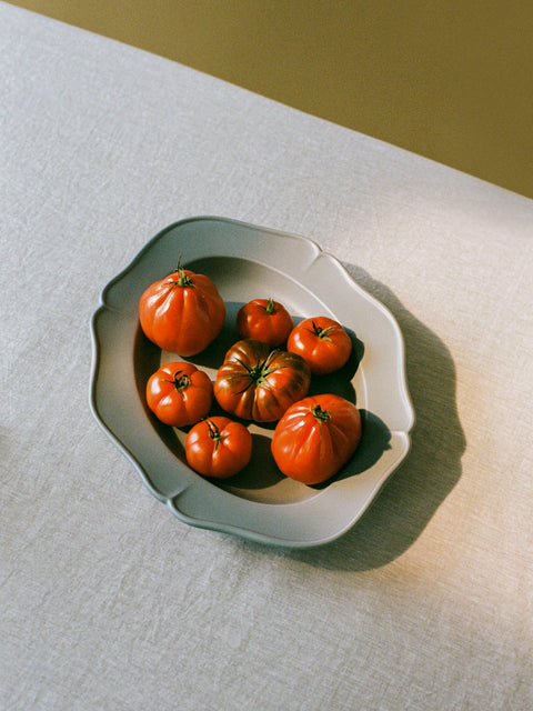 A decorative light blue bowl with seven fresh tomatoes on beige linen tablecloth. 
