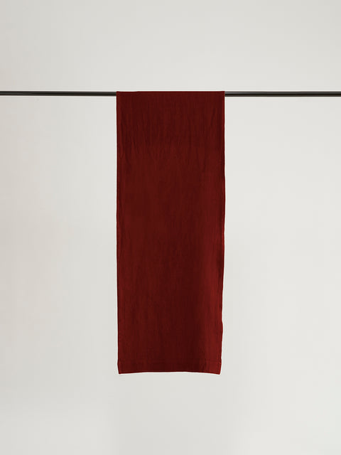 A dark red linen table runner hanging over black rod in front of grey background. 